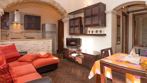 Una sala acogedora con chimenea de piedra, armarios de madera oscura, un televisor de pantalla plana y una mesa de comedor con mantel floreado.