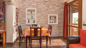 Un comedor con pared de ladrillo, dos estantes de vidrio y una mesa con mantel floreado.