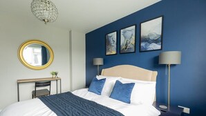Quarto com cama, escrivaninha, cadeira, espelho e duas luminárias fixadas na parede.