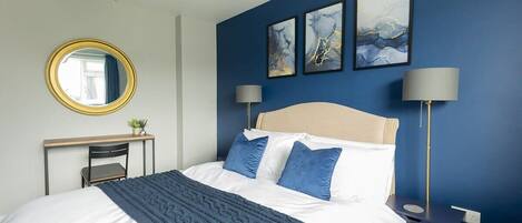 Een slaapkamer met een bed, een bureau, een stoel, een spiegel en twee wandlampen.