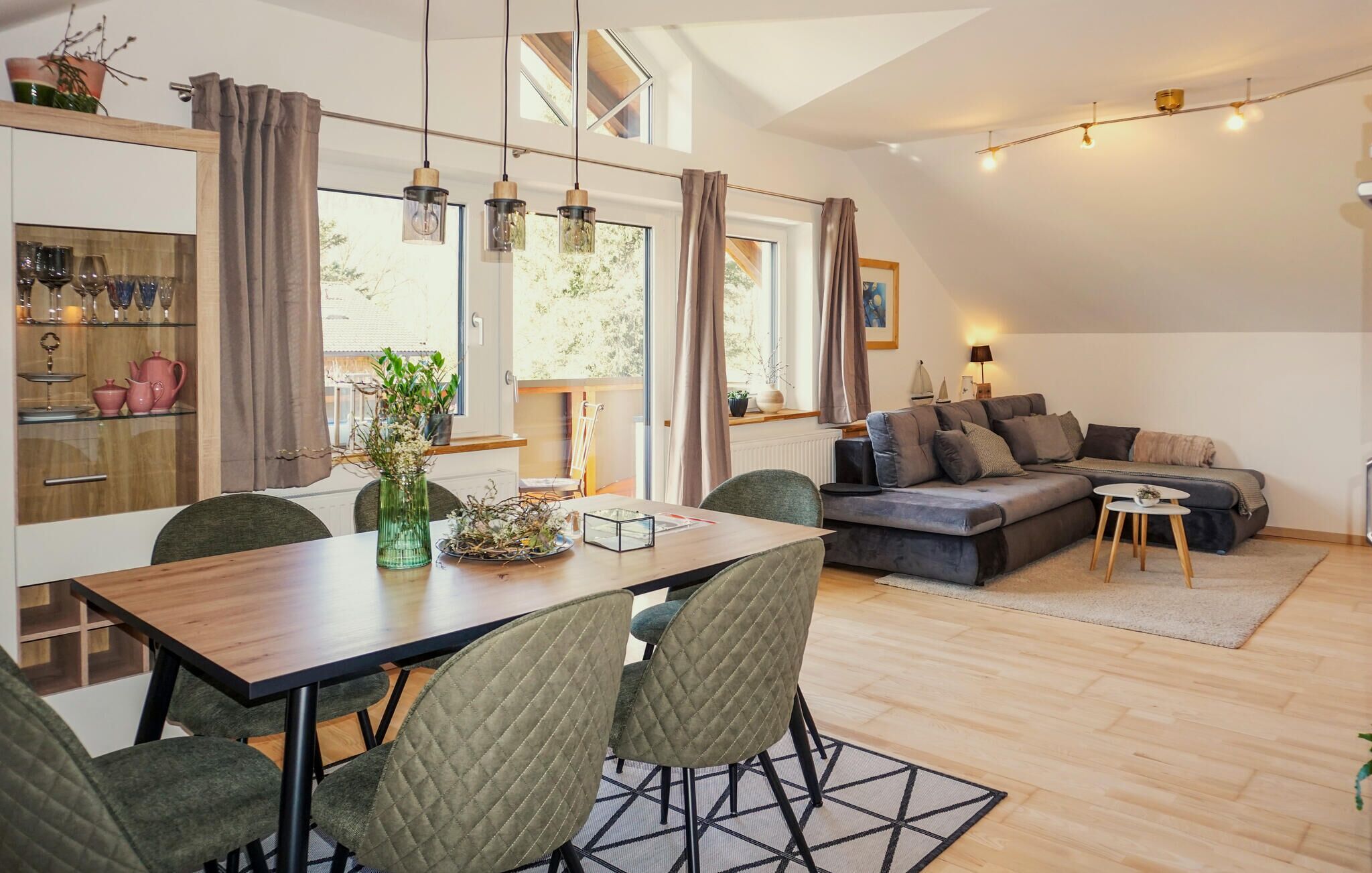 A modern living room with a sofa, dining table, chairs, and a kitchen area with cabinets and a window.