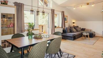 A modern living room with a sofa, dining table, chairs, and a kitchen area with cabinets and a window.