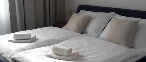 A neatly made double bed with white linens, a dark headboard, and a framed picture on the wall.