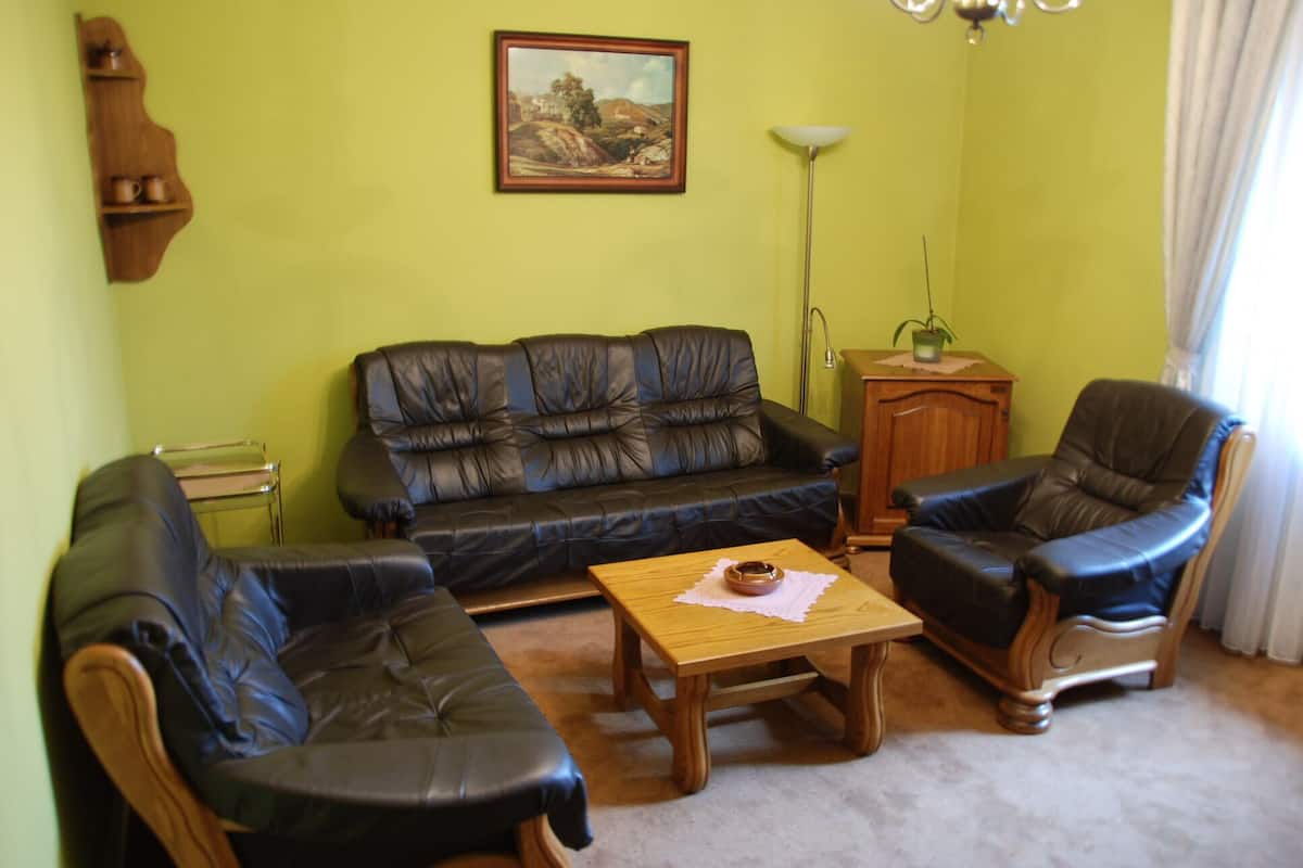 Una sala de estar con un sofá, sillones, una mesa de centro de madera, una lámpara y un cuadro en la pared.