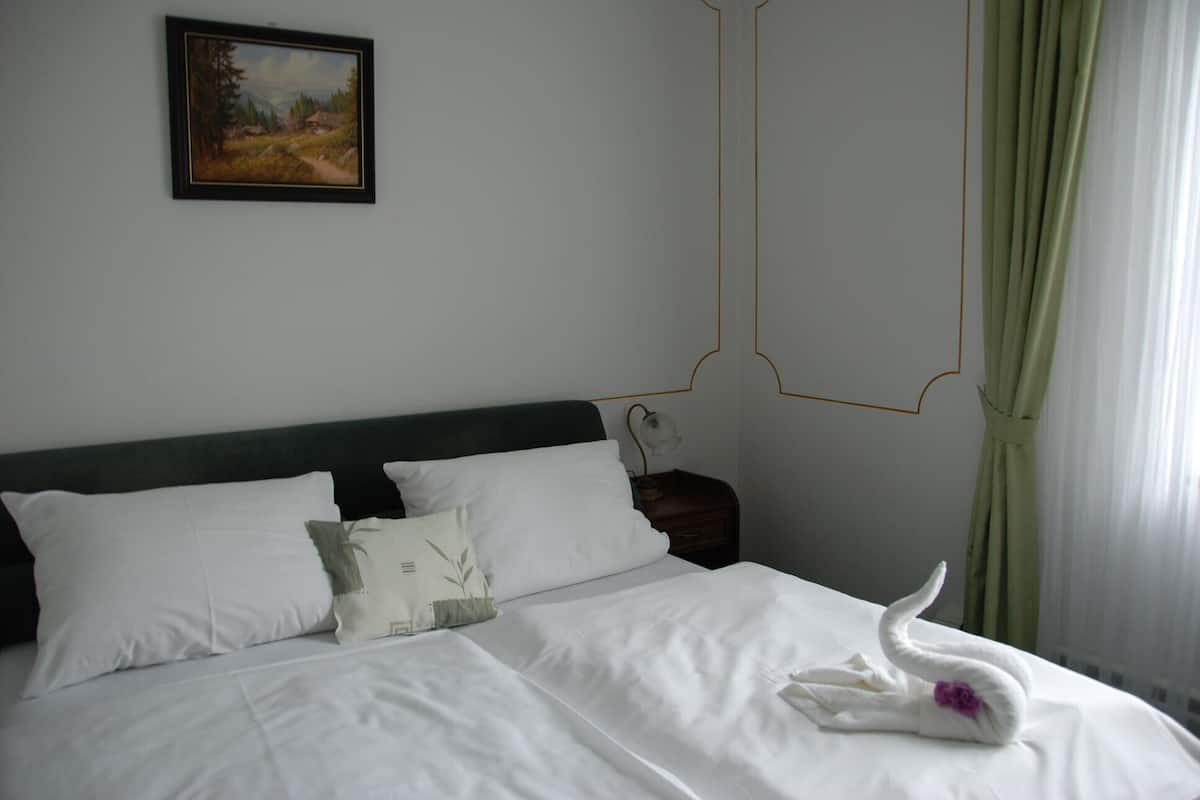 Una cama bien hecha con sábanas blancas, una toalla con forma de cisne y un cuadro en la pared.