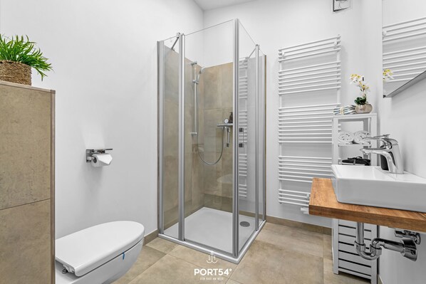 A modern bathroom with a glass-enclosed shower, white fixtures, and a wooden vanity.