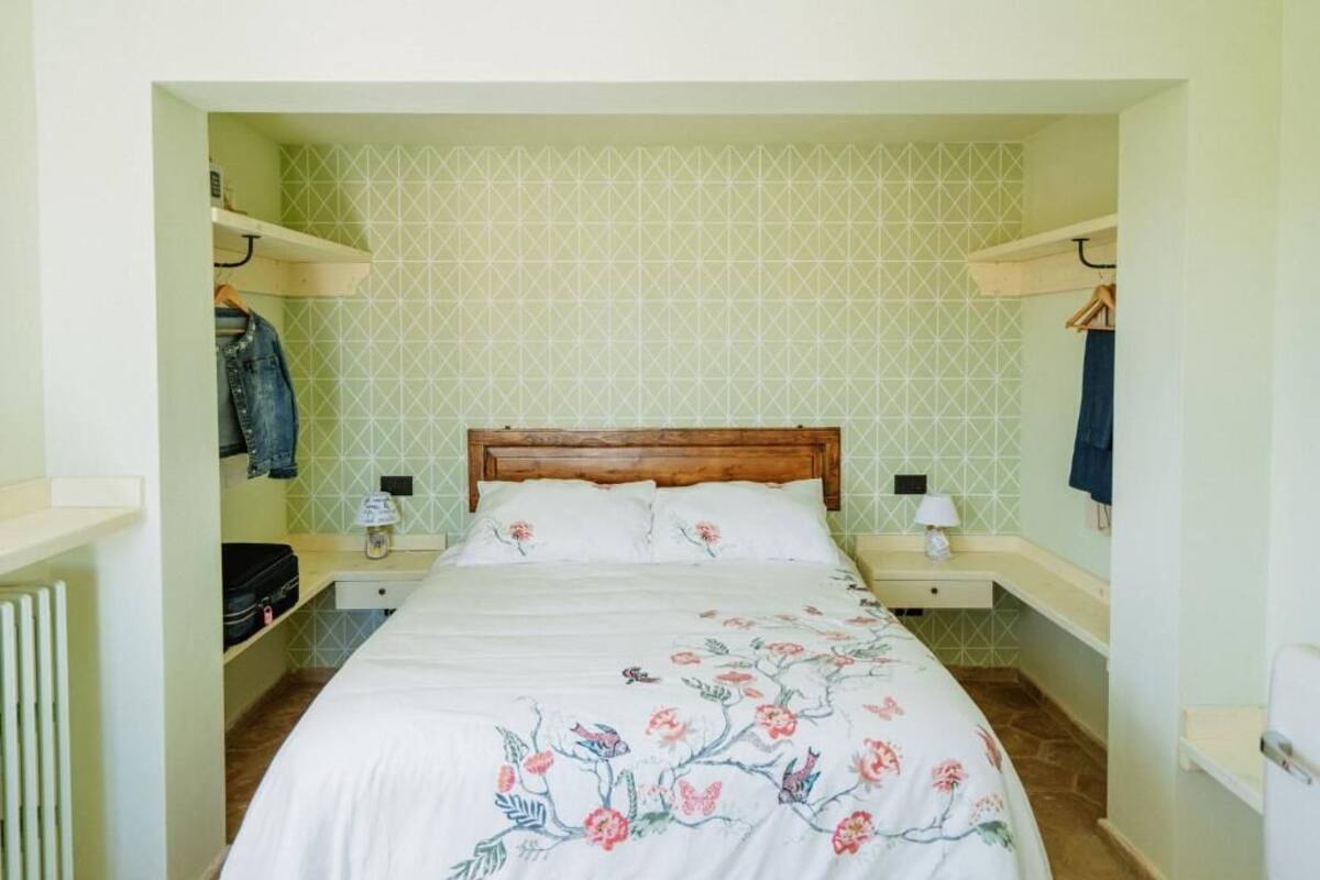 A bedroom with a wooden bed, floral bedding, two bedside tables with lamps, and a geometric patterned wall.
