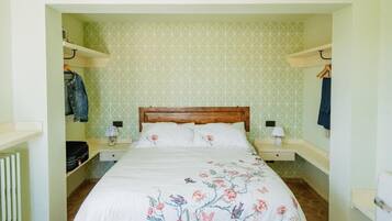 A bedroom with a wooden bed, floral bedding, two bedside tables with lamps, and a geometric patterned wall.