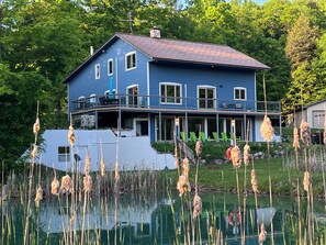 Una casa a due piani con un balcone, una piscina e uno stagno con giunchi.