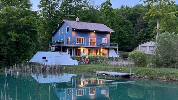 Una casa con un muelle que se adentra en un lago tranquilo, rodeada de árboles frondosos.