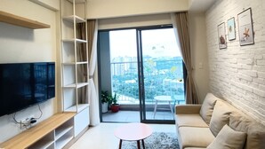 A modern living room with a flat-screen TV, a sofa, a coffee table, and a balcony with a city view. - Masteri Thao Dien Apartment  Quan 2 (Ho Chi Minh City)