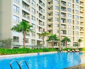 A modern apartment building with a swimming pool, palm trees, and lounge chairs. - Masteri Thao Dien Apartment  Quan 2 (Ho Chi Minh City)
