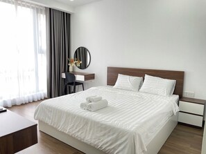 A hotel room with a large bed, a desk with a chair, a round mirror, and a view of the outside through sheer curtains. - Masteri Thao Dien Apartment  Quan 2 (Ho Chi Minh City)