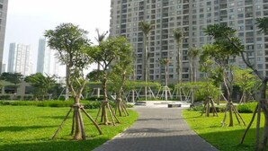 A pathway leading to a high-rise building with a modern design, surrounded by well-maintained greenery and palm trees. - Masteri Thao Dien Apartment  Quan 2 (Ho Chi Minh City)