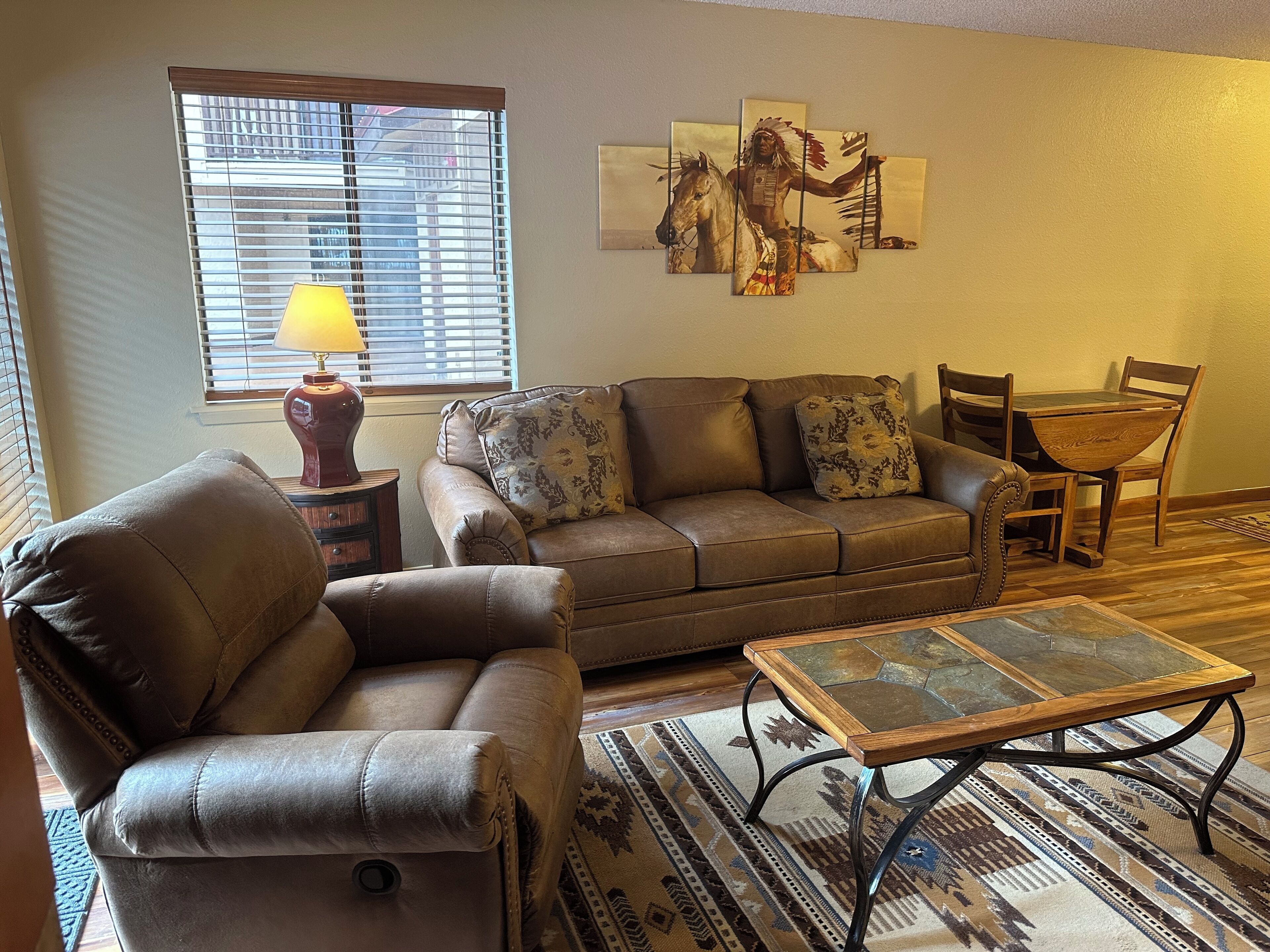 A living room with a sofa, armchair, coffee table, and a painting on the wall.