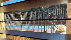 A view of a swimming pool with a metal fence, wooden deck, and a clear sky.