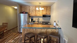 A kitchen with wooden cabinets, a stainless steel refrigerator, a microwave, a stove, and a glass island with stools.