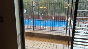 A view of a swimming pool through a metal fence with a wooden deck in the foreground.
