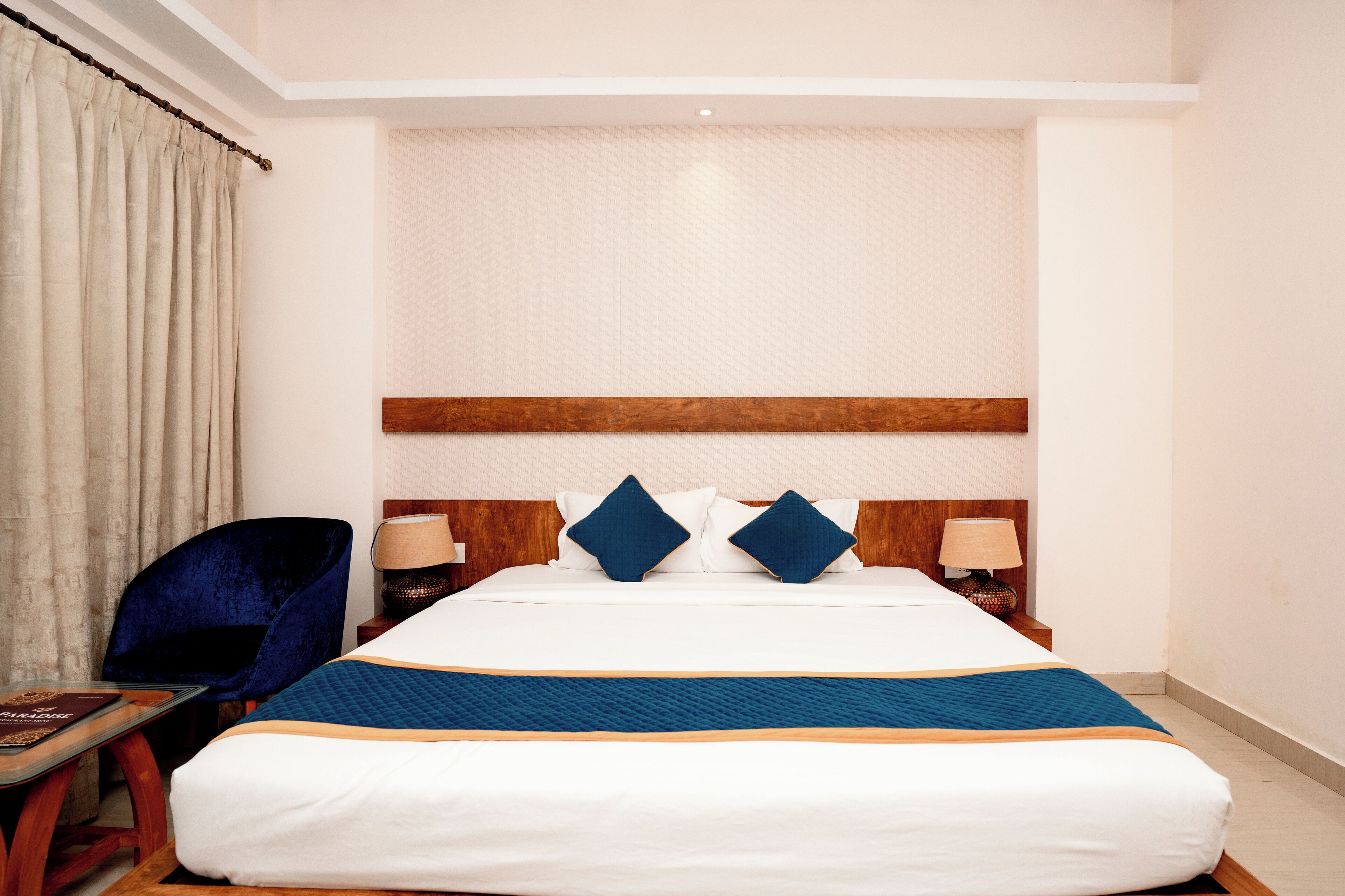 Una habitación de hotel con una cama grande, dos mesitas de noche, una silla y una cortina.