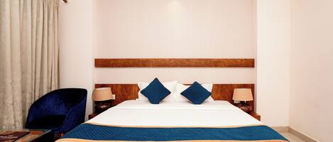 Una habitación de hotel con una cama grande, dos mesitas de noche, una silla y una cortina.