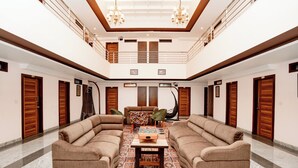 A spacious, well-lit lobby with a high ceiling, a central seating area with sofas, a patterned rug, and wooden doors.