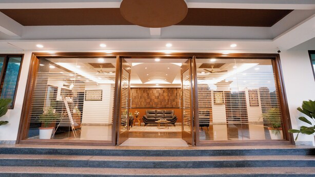 A modern hotel entrance with a glass door, a wooden interior, and a staircase leading up.