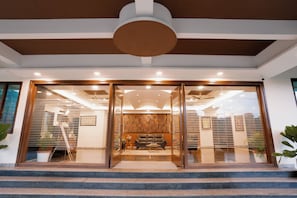 A modern hotel entrance with a glass door, a wooden interior, and a staircase leading up.