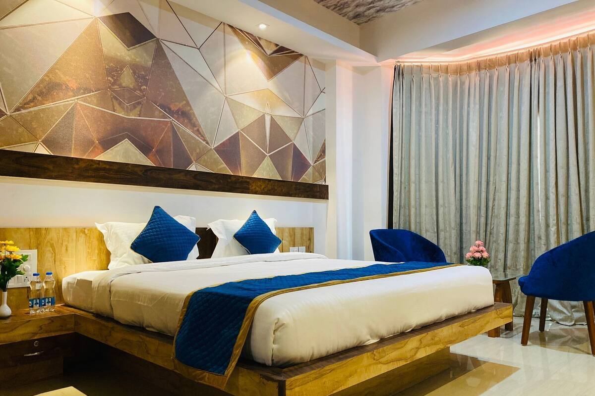 A modern hotel room with a large bed, wooden headboard, and a geometric wall design.