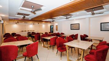 Une salle de conférence dotée de plusieurs tables et de chaises rouges, équipée de ventilateurs de plafond et d’un système d’éclairage encastré.