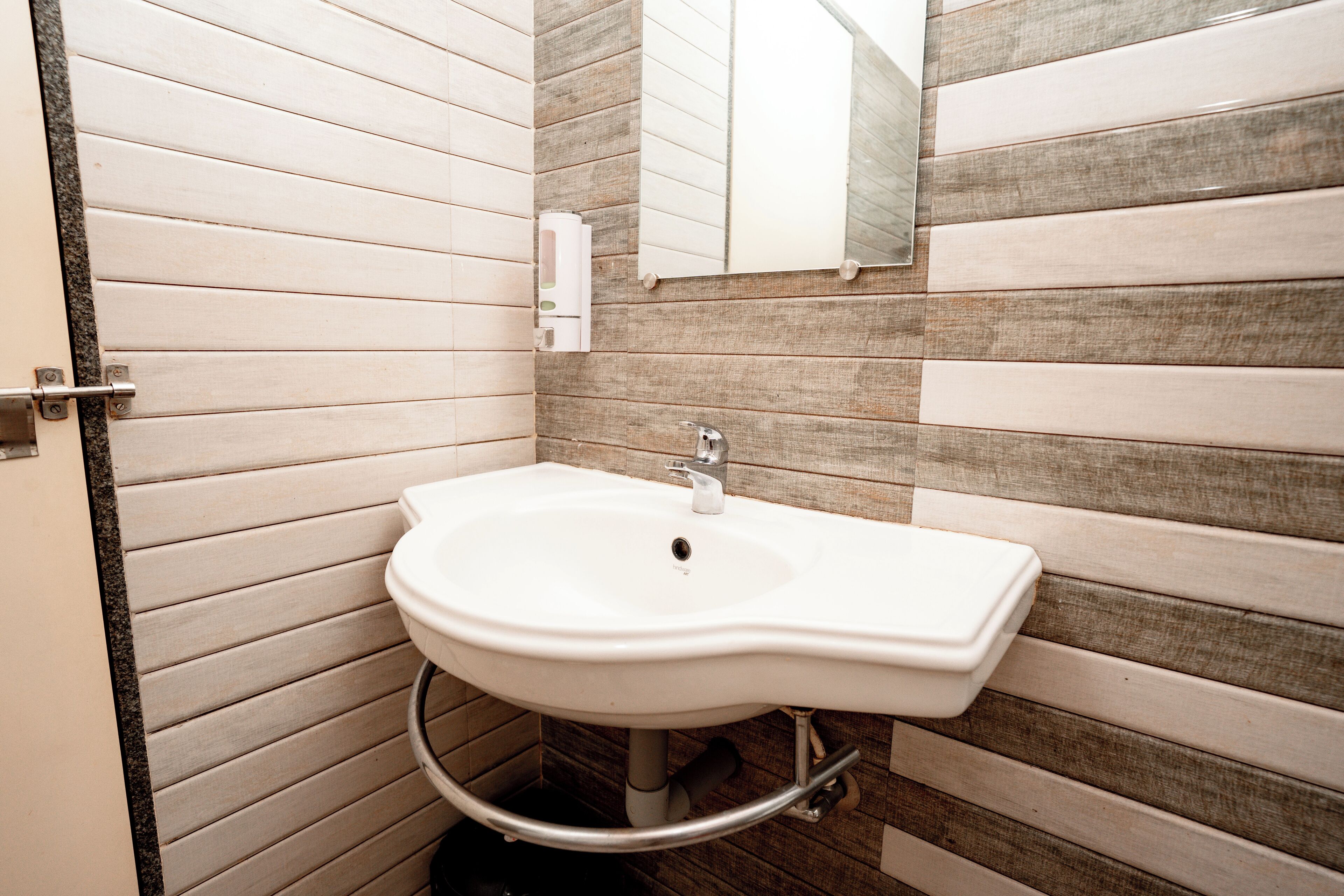 A bathroom with a white sink, a mirror, and a towel dispenser.