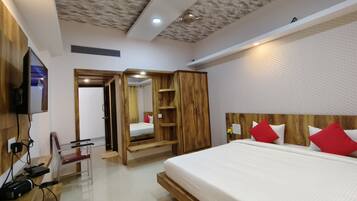Una habitación de hotel moderna con cabecera de madera, una cama grande con almohadas rojas, un armario de madera, un espejo y un televisor montado en la pared.