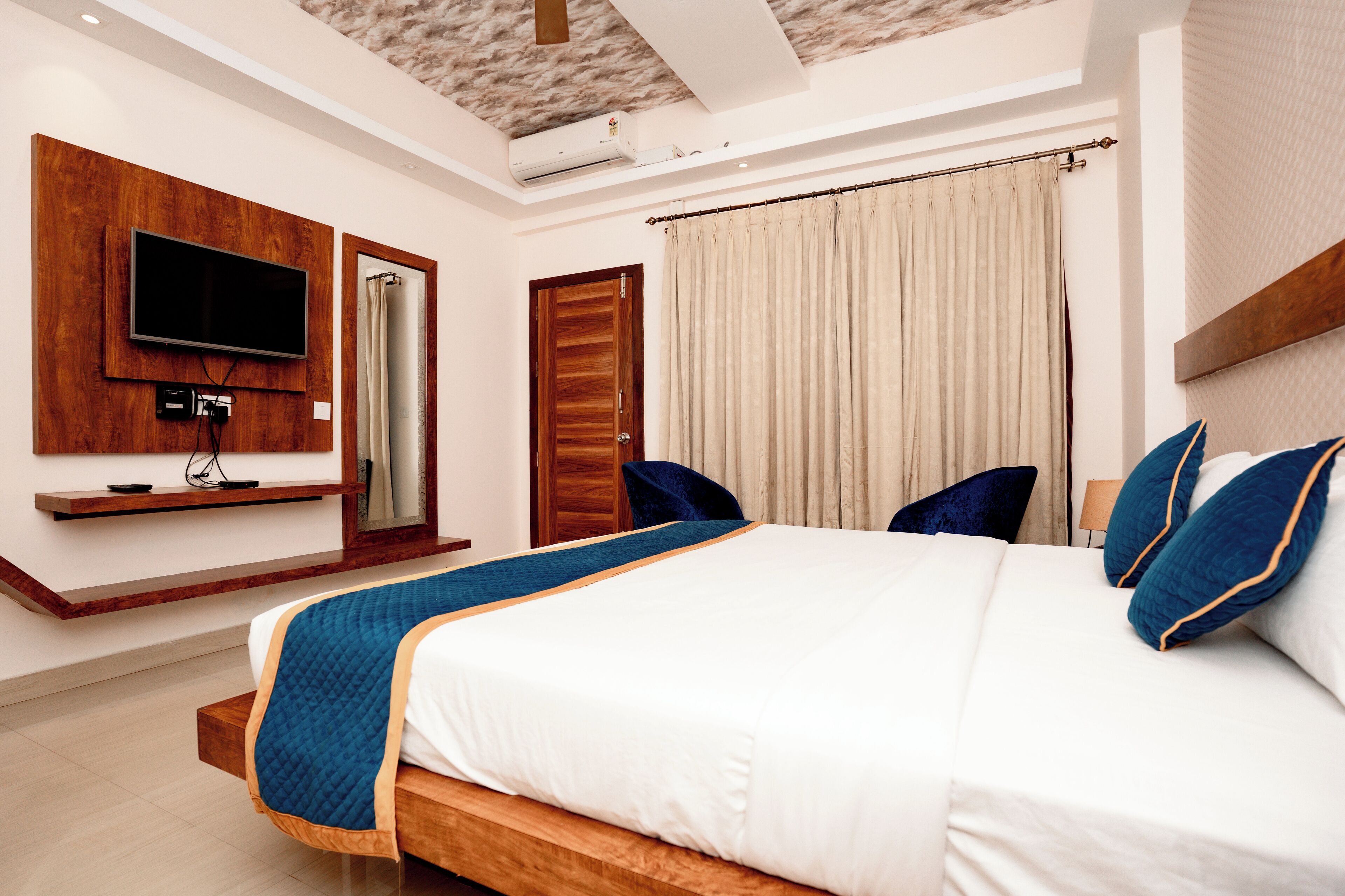A modern hotel room with a large bed, a flat-screen TV mounted on the wall, a wooden headboard, and a ceiling fan.