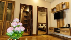 A hotel room with wooden flooring, a bed with white bedding, a TV mounted on the wall, and a small wooden cabinet.