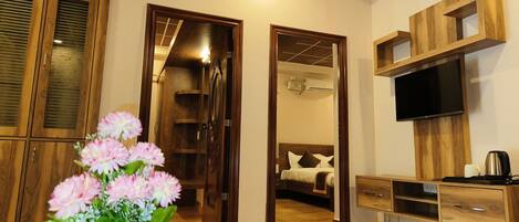 A hotel room with wooden flooring, a bed with white bedding, a TV mounted on the wall, and a small wooden cabinet.