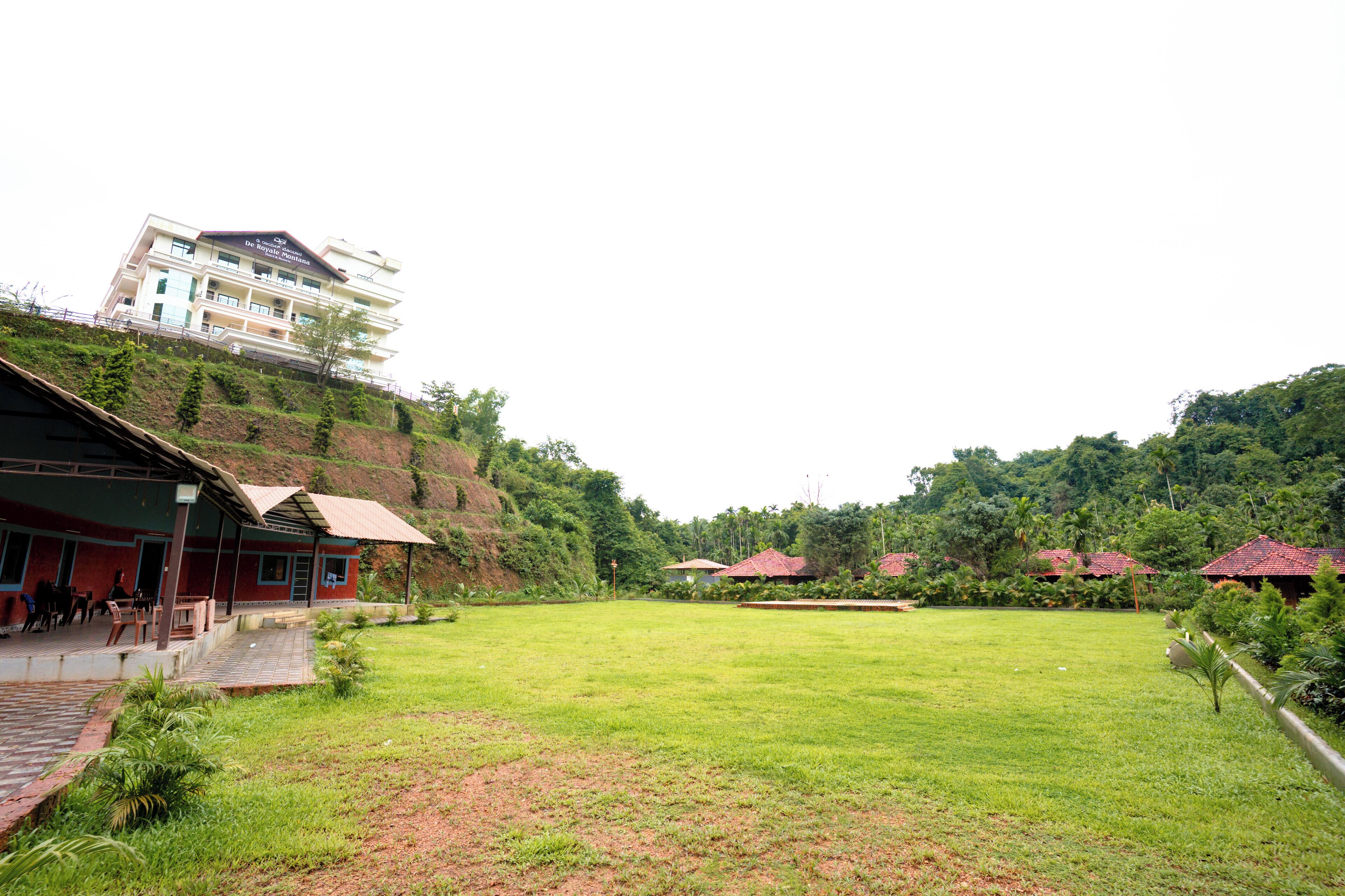 A hotel with a large grassy lawn, a covered outdoor seating area, and a building with a red roof.