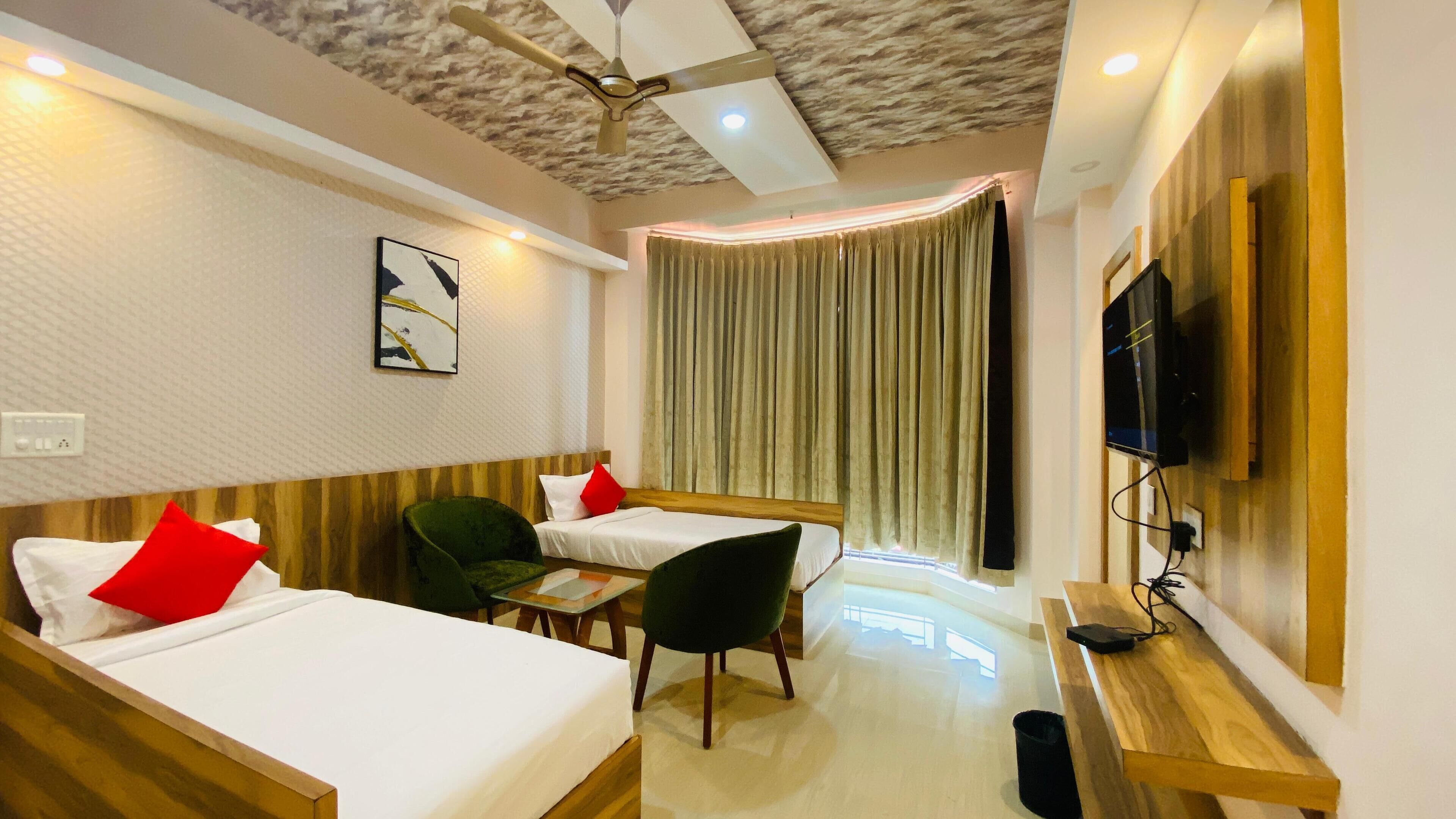 A hotel room with two single beds, a desk, a chair, a TV, and a ceiling fan.