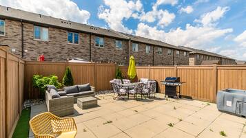 Une terrasse à l’arrière de la maison, avec des meubles d’extérieur, un barbecue et une clôture en bois.