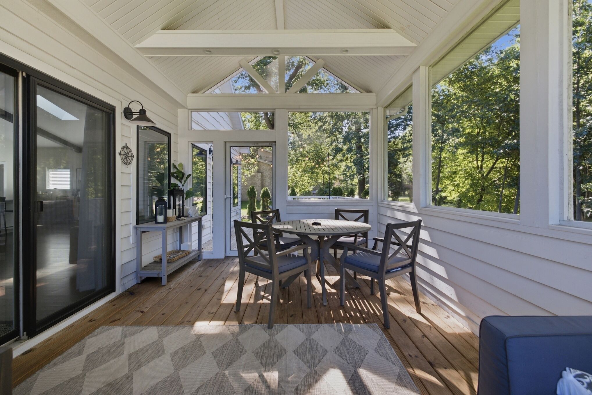 A covered patio with a table and chairs, a bench, and a view of trees.