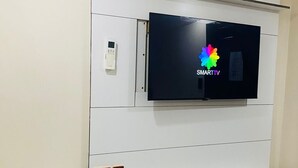 A flat-screen TV mounted on a white wall with a built-in bench below. - DBright Guest Lodge (Pretoria)