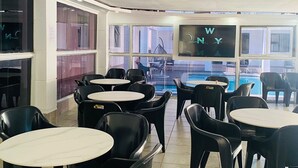 A restaurant with black plastic chairs and round tables, large windows, and a view of a pool. - DBright Guest Lodge (Pretoria)