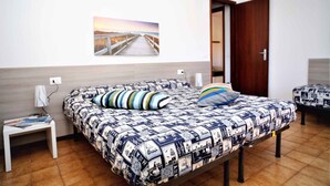 A bedroom with a bed, a nightstand, a wall-mounted picture, and a door. - Holiday apartment mit Klimaanlage und Balkon (Lignano)