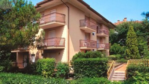 A multi-story building with balconies, surrounded by greenery and a staircase leading to the entrance. - Holiday apartment mit Klimaanlage und Balkon (Lignano)