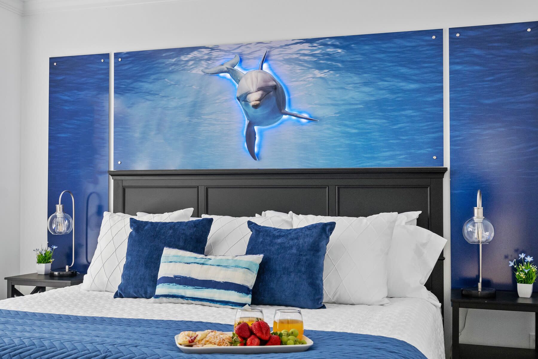 A hotel room with a bed, a nightstand, a wall-mounted lamp, and a wall art of a dolphin.