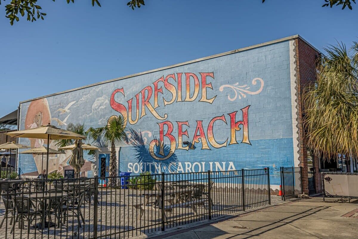 Un mural de 'Surfside Beach' con mesas al aire libre y una valla.