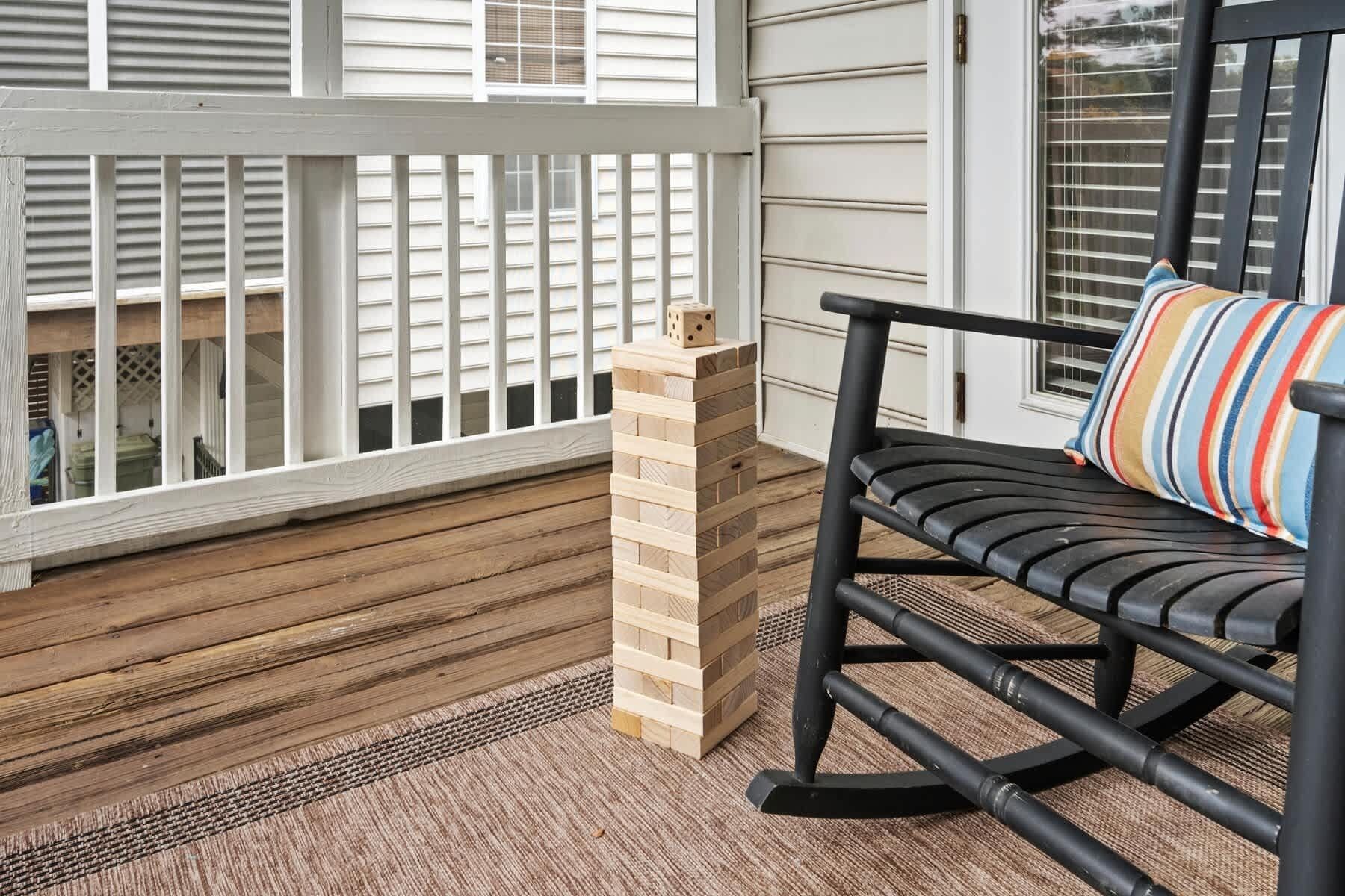 A wooden deck with a black rocking chair and a striped pillow.