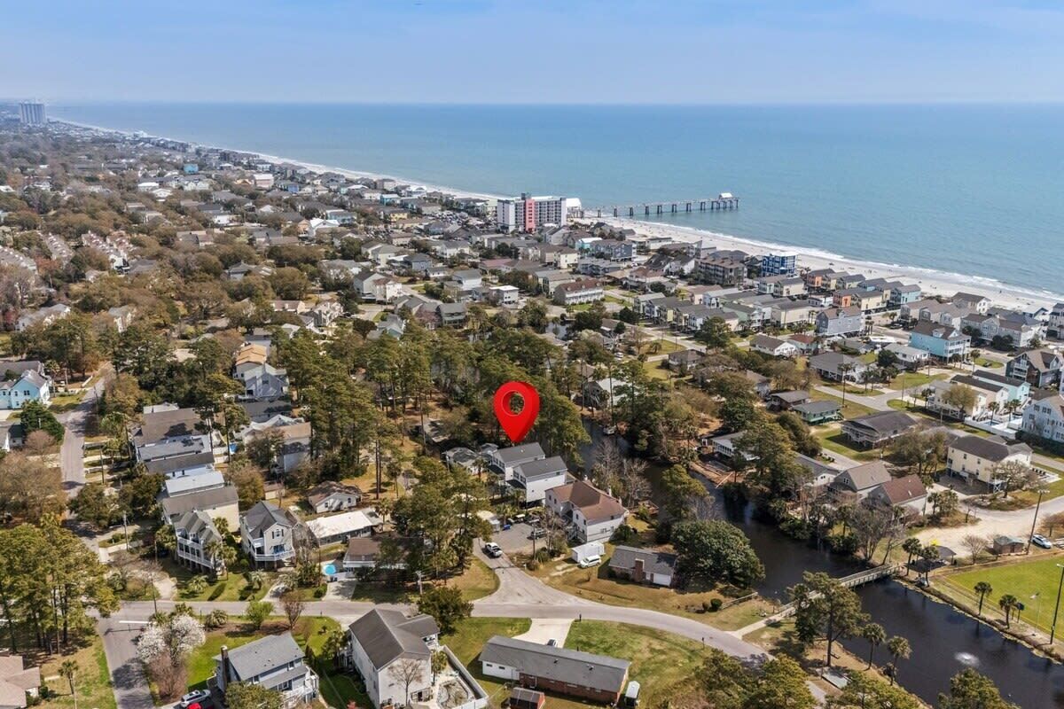 An aerial view of a coastal residential area with houses, a pier, and a beach.