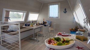 A modern, well-lit room with a dining table set for two, a bunk bed, and a large window with curtains. - Holiday home with air conditioning and terrace (Lignano Sabbiadoro)