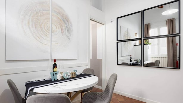 Una habitación moderna con una mesa redonda, sillas tapizadas en gris, un cuadro abstracto grande y un espejo con diseño de tres paneles.