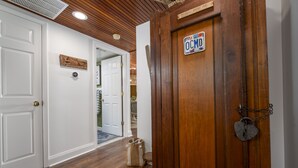 Un pasillo con suelo de madera, puertas blancas y una puerta de madera con un candado con forma de corazón.