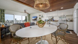 Una cocina moderna con armarios blancos, un comedor con sillas de mimbre y un ventanal con vistas a un paisaje urbano.